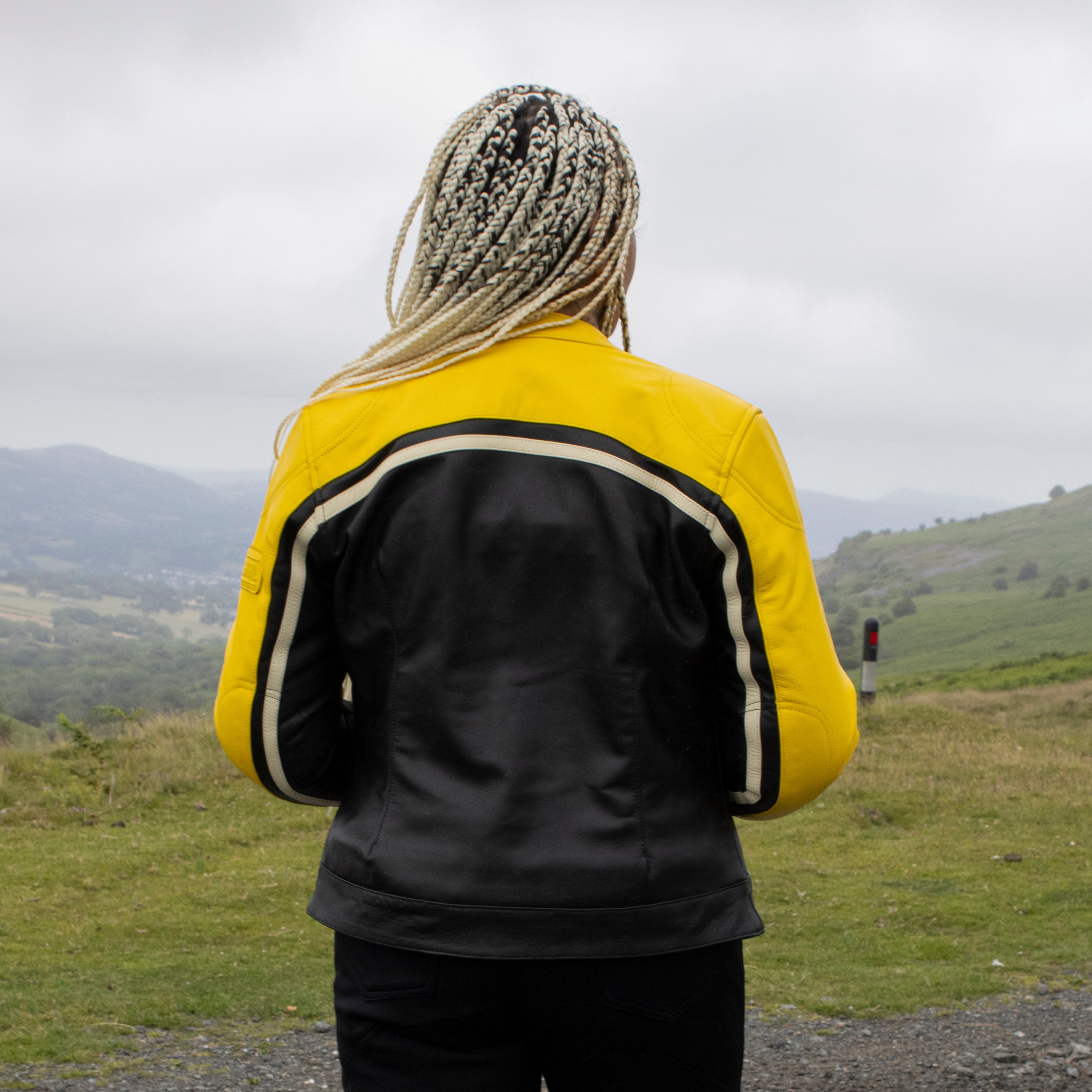 Person wearing a black and yellow jacket standing on a road with a scenic background